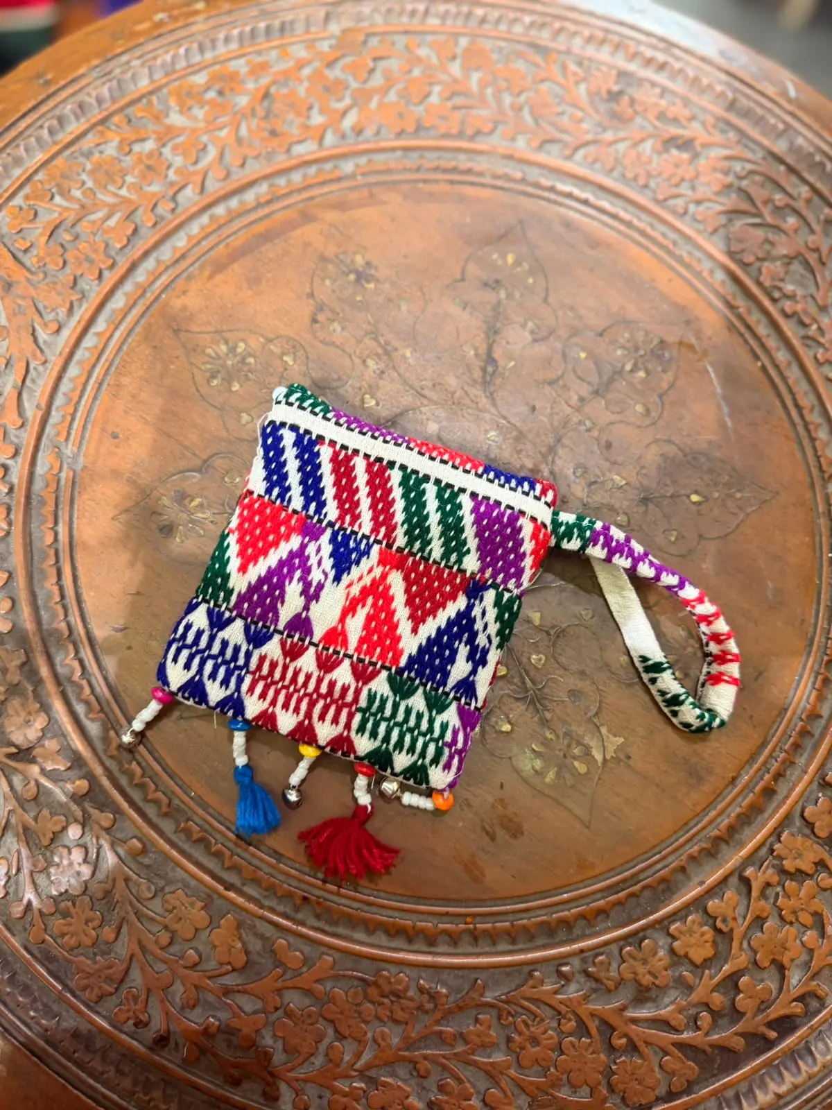 Multicolour Kutchi traditional mobile pouch with tassel detailing on a carved copper table