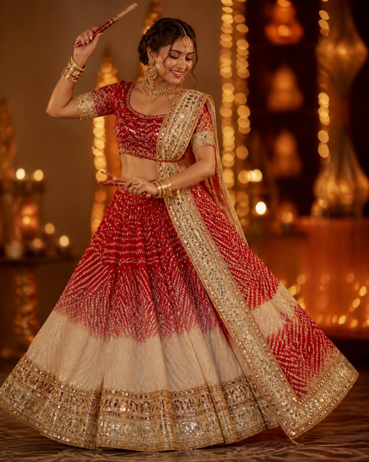 Woman in a red and ivory bandhani chaniya choli dancing with dandiya sticks