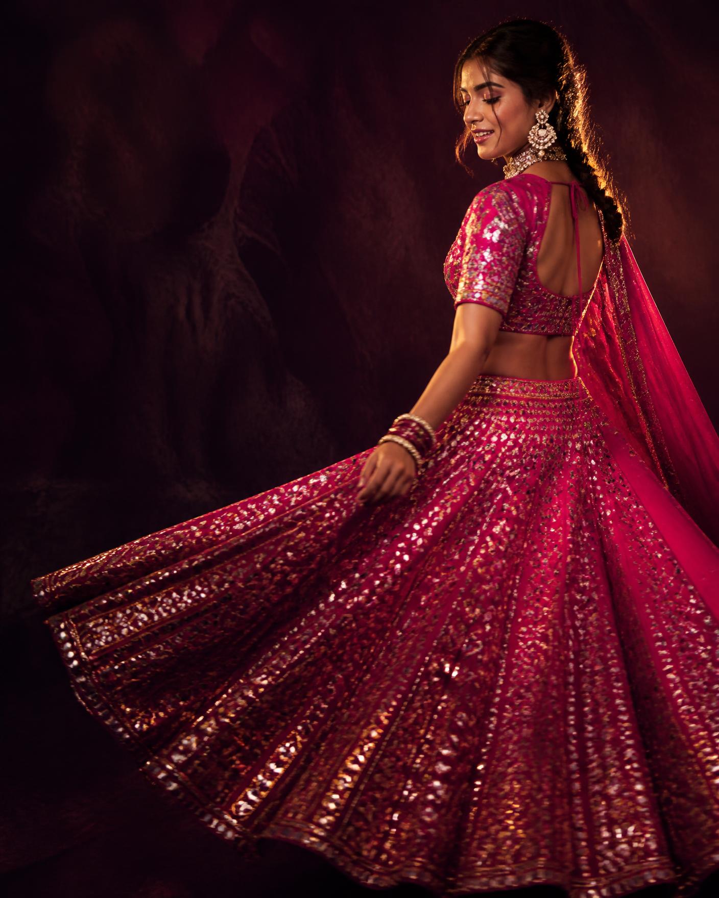 Woman twirling in a magenta and gold mirror work chaniya choli against a deep plum backdrop